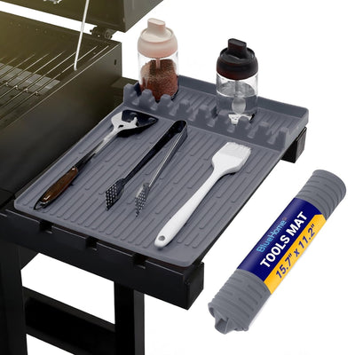 Grey silicone grill tool mat resting on a barbecue side shelf with grilling utensils and seasoning jars.
