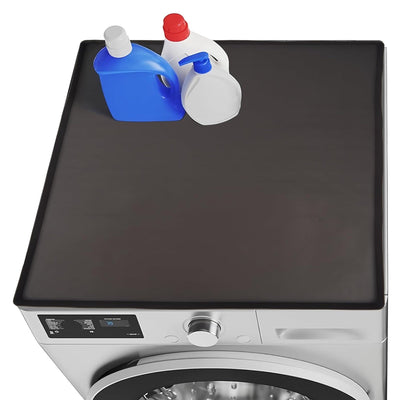 Black silicone washer and dryer top mat with raised edges installed on a front load machine with laundry bottles.