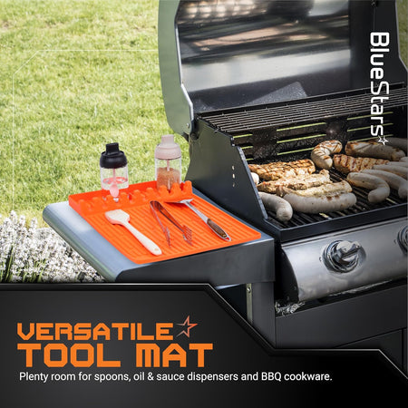 Orange silicone griddle mat holding BBQ tools and condiment dispensers on a grill side shelf.